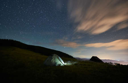 Front view of scenery of tourist tent near forest under starry sky. Somebody is camping in mountains...