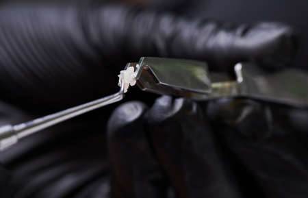 Close up view. Orthodontist in black gloves putting adhesive paste by stainless steel dental tool on orthodontic bracket for attaching braces to teeth. Concept of dentistry, orthodontic treatmentの写真素材
