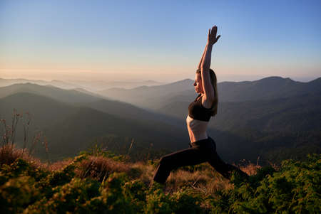 Side view of slim woman in black sportswear stretching on nature. Concept of harmony with freedom...