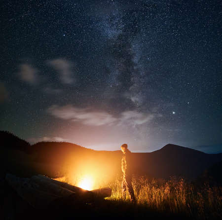 Side view of man standing and enjoying near fire and relaxing under starry sky. Concept of incredible view sky with beautiful stars.の写真素材