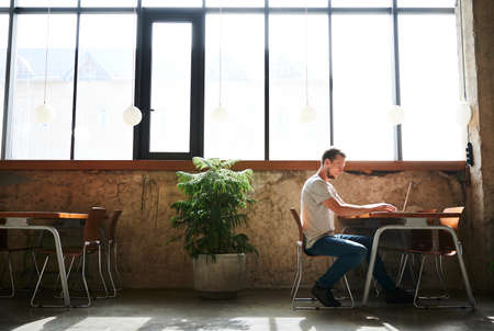 Male student typing on laptop in cafe. Man sitting by table in coffee house and working on laptop. Concept of modern lifestyle.の写真素材
