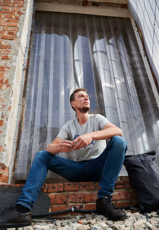 Below view of smiling male sitting on stairs of abandoned house. Young man is resting on stairs outdoor. Concept of leisure.の写真素材
