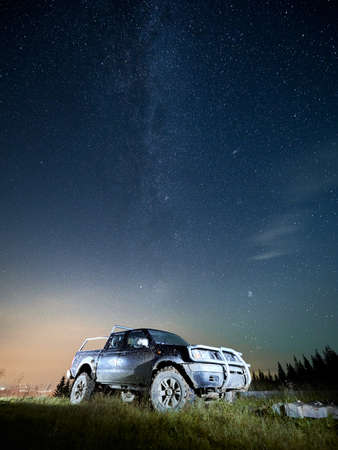 Night mountain valley with vehicle under beautiful blue sky with stars. Magnificent view of night...