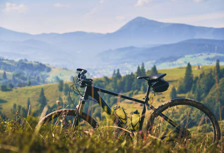 Picturesque snapshot of bicycle in the mountains. Beautiful natural landscape: mountain peak, green hills, evergreen spruces, meadow with wildflowers in summer.の写真素材