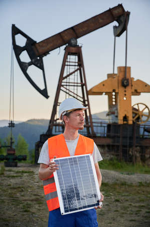 Oilman in construction helmet looking to the right, keeping one solar battery as alternative to oil...