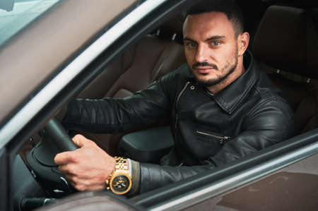 Portrait of handsome young man driving modern car. Guy driver wearing casual clothes and gold watch.の写真素材