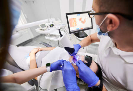 Dentist and his assistant scanning patients teeth with modern scanning machine. Digital print of patients teeth is on big screen. Modern high precision technologies. Concept of digital dentistryの写真素材