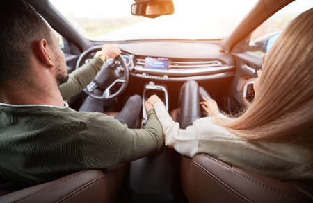 Top view of pair in love in cabin of luxury car. Man driver and his girlfriend on front passenger seat holding each others hand tightly. Romantic moments of two lovers while riding automobile.の写真素材