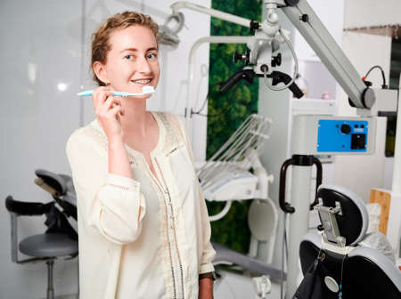 Portrait of a beautiful woman in well equipped dentists office demonstrating teeth brushing. Young...