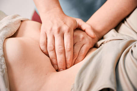 Close up of physician hands massaging woman abdomen during medical examination. Professional doctor examining patient stomach in clinic. Concept of healthcare and therapeutic massage.の写真素材