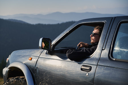 Against the backdrop of forest and mountain hills in distance, view of SUV driver leaning with one...