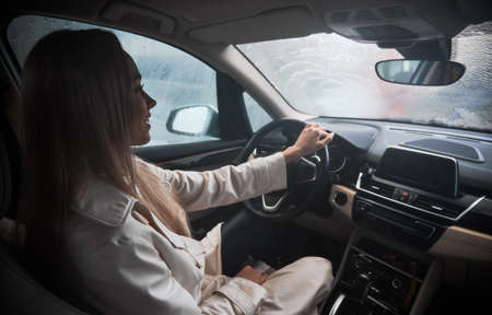 Beautiful smiling woman client sitting in the car on carwash station. Worker cleaning automobile, using high pressure water.の写真素材