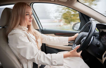Beautiful young woman driving modern car. View from inside a car. Blonde driver wearing casual...