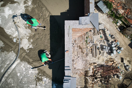 Two men builders screeding floor at construction site. Top view of male worker standing near...