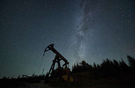 Operation of oil pump in borehole at night time under beautiful starry sky. Pumping natural fuel by rod pump from bowels of the earth.の写真素材