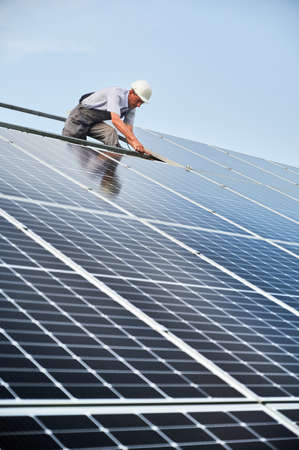 Male worker mounting photovoltaic solar panel system outdoors. Man engineer placing solar module on...