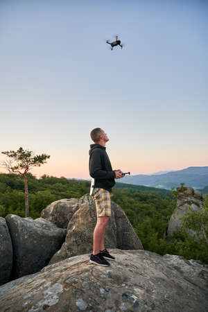 Man operating drone using remote controller. Man using drone at sunset for photos and video making while standing on top of high boulder in the mountains.の写真素材