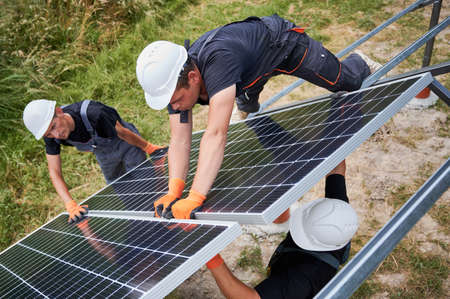 Male workers building photovoltaic solar panel system outdoors. Men engineers placing solar module...