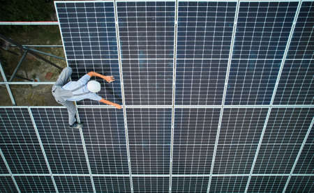 Male worker in safety helmet installing photovoltaic solar panel. Man technician assembling solar...