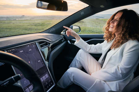 POV young business woman sitting in passenger seat next to driver and pointing finger in front of...