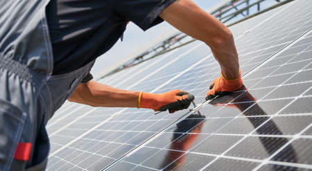 Cropped view of man hands in work gloves mounting photovoltaic solar panels. Worker assembling solar...