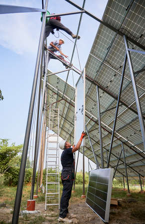 Male workers building photovoltaic solar panel system outdoors. Men electricians lifting solar...