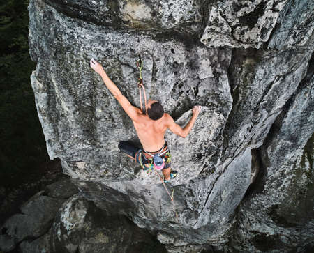 Young man climber climbing difficult route on high boulder with rope. Fearless rock climber training rock climbing on summer day. Concept of extreme sport, adventures and active lifestyle. Aerial viewの写真素材