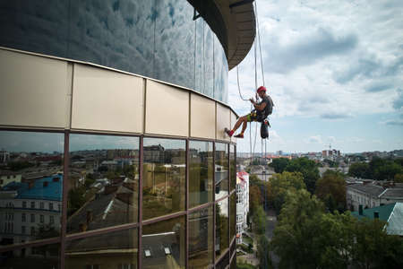 Industrial mountaineering worker cleaning glass window of high-rise building. Male cleaner using...