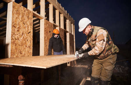Carpenter using circular saw for cutting wooden OSB board. Man worker building wooden frame house on...