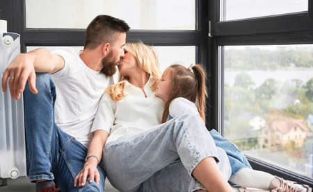 Man and woman sitting on the floor and kissing each other. Happy loving family sitting by the window...