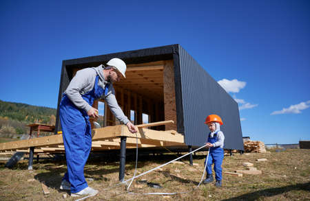 Father with toddler son building wooden frame house on pile foundation. Boy helping his daddy,...