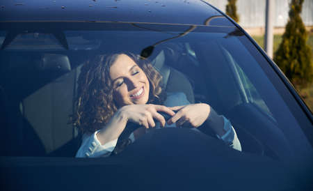 Beautiful businesswoman with closed eyes sitting in electric car and smiling while using vehicle...