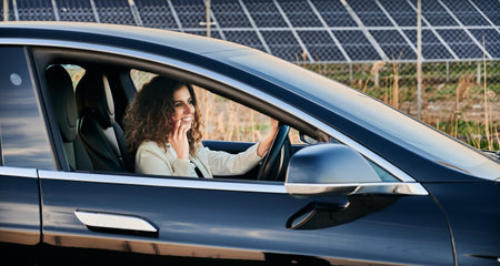 Happy businesswoman using 4g wireless in roaming for making international mobile conversation and discussing solar panels, cheerful female driver calling via smartphone app for talking about vehicle.の写真素材