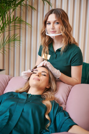 Portrait of beauty specialist comping client eyelashes after extension procedure. Female eyelashes...