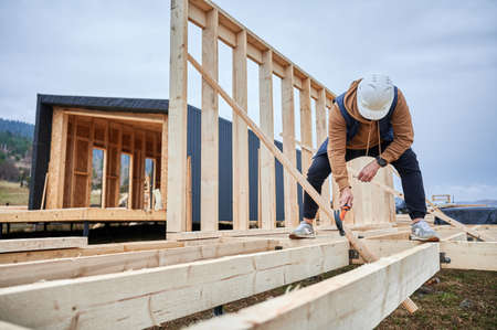 Man worker building wooden frame house on pile foundation. Carpenter hammering nail into wooden...