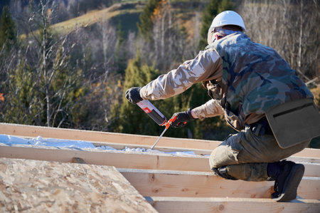 Male builder doing thermal insulation on roof of wooden frame house. Man worker spraying...