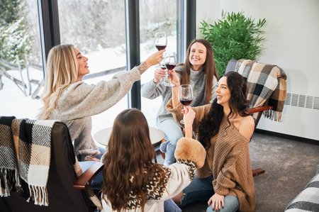 Young women enjoying winter weekends inside contemporary barn house. Four girls having fun and clinking glasses with red wine.の写真素材