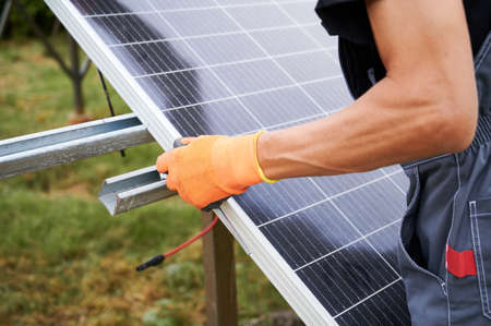 Close up of man engineer installing solar modules. Male worker in work gloves mounting solar photovoltaic panel system.の写真素材