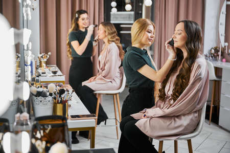 Makeup artists doing professional makeup for women in visage studio. Young woman beauty specialist...