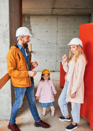 Man giving apartment keys to wife while little girl looking to the camera. Parents with daughter standing in building under construction. Happy family life and property purchase concept.の写真素材