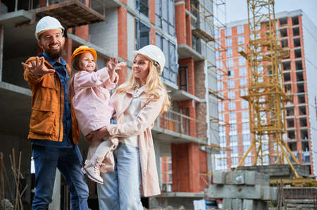 Man, woman and child standing outside building under construction. Happy family homeowners posing on the street at construction site.の写真素材