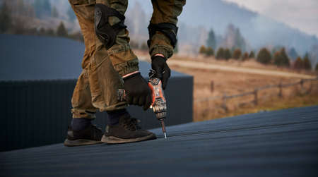 Male builder installing black corrugated iron sheet used as facade of future cottage. Man worker building wooden frame house. Carpentry and construction concept.の写真素材