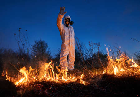 Fireman ecologist showing stop sign while working in field with wildfire at night. Man in protective...