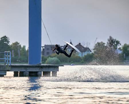 Wakeboarder making tricks while wakeboarding on lake. Young man surfer having fun wakesurfing in the cable park. Water sport, outdoor activity concept.の写真素材