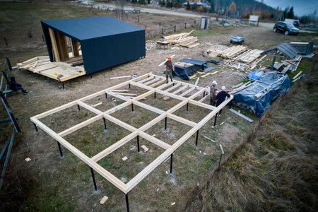 Men workers building wooden frame house on pile foundation. Carpenters installing wooden joist. Carpentry concept.の写真素材