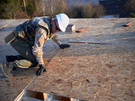 Carpenter mounting wooden OSB board on rooftop of future cottage. Man worker building wooden frame house. Carpentry and construction concept.の写真素材