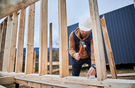 Man worker building wooden frame house on pile foundation. Carpenter hammering nail into wooden plank, using hammer. Carpentry concept.の写真素材