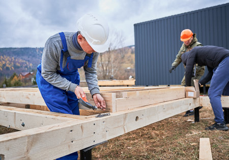 Man worker building wooden frame house on pile foundation. Carpenter hammering nail into wooden plank, using hammer. Carpentry concept.の写真素材