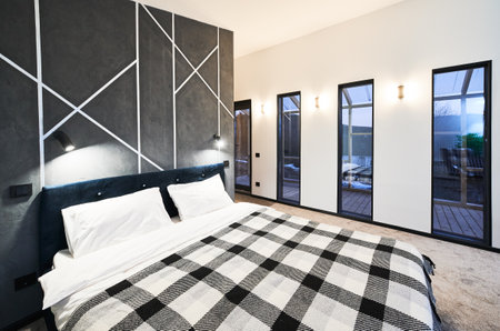 Contemporary bedroom with numerous glass doors leading to terrace at dusk. Side view of illuminated...