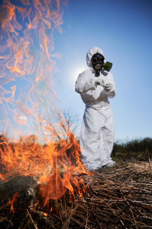 Unrecognizable person burning old dried grass in field. Ecologist holding matchbox and setting fire...